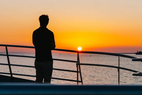 Ein Mann blickt von der Reling des MS Sonnenkönigin in den Sonnenuntergang
